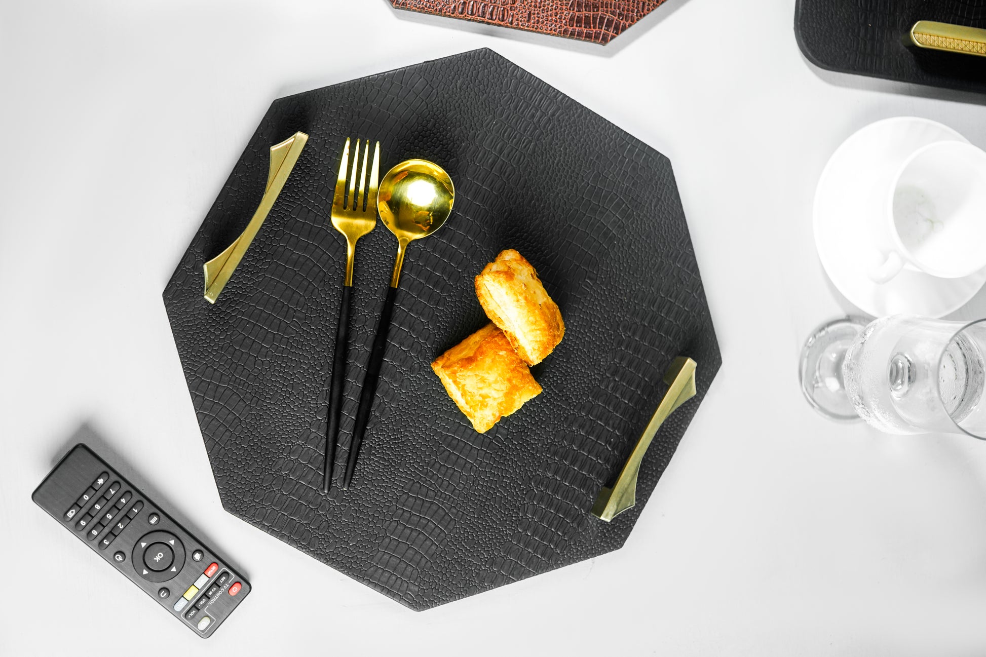 Top view of a black octagon serving tray with a spoon and two biscuits, showcasing the tray's elegant design and the golden-colored handles. The image is clear, emphasizing the tray and its contents.