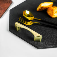 Close-up from the side of a black octagon serving tray, highlighting the golden-colored handles. The focus is on the elegant handles and the tray's design.