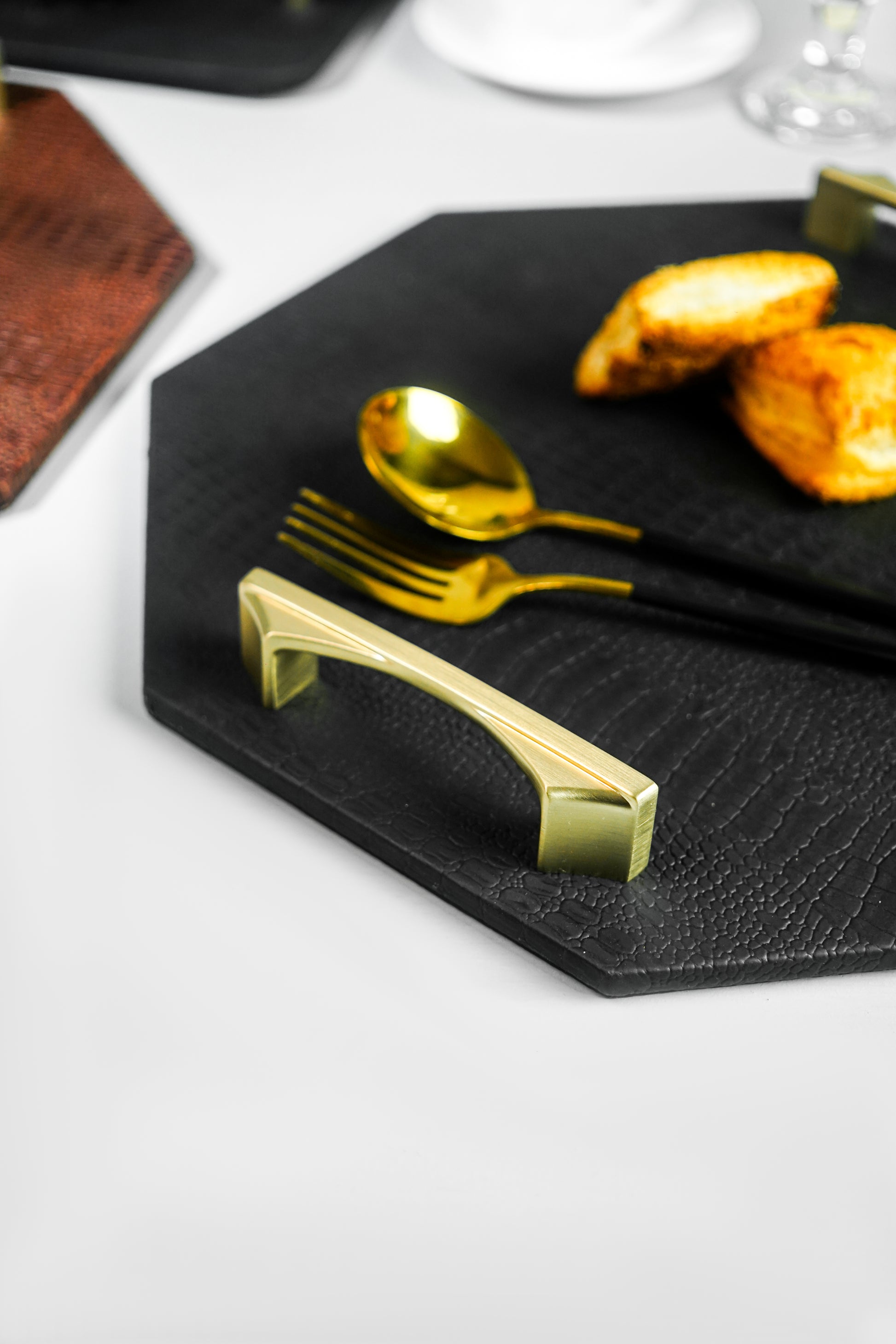 Close-up from the side of a black octagon serving tray, highlighting the golden-colored handles. The focus is on the elegant handles and the tray's design.