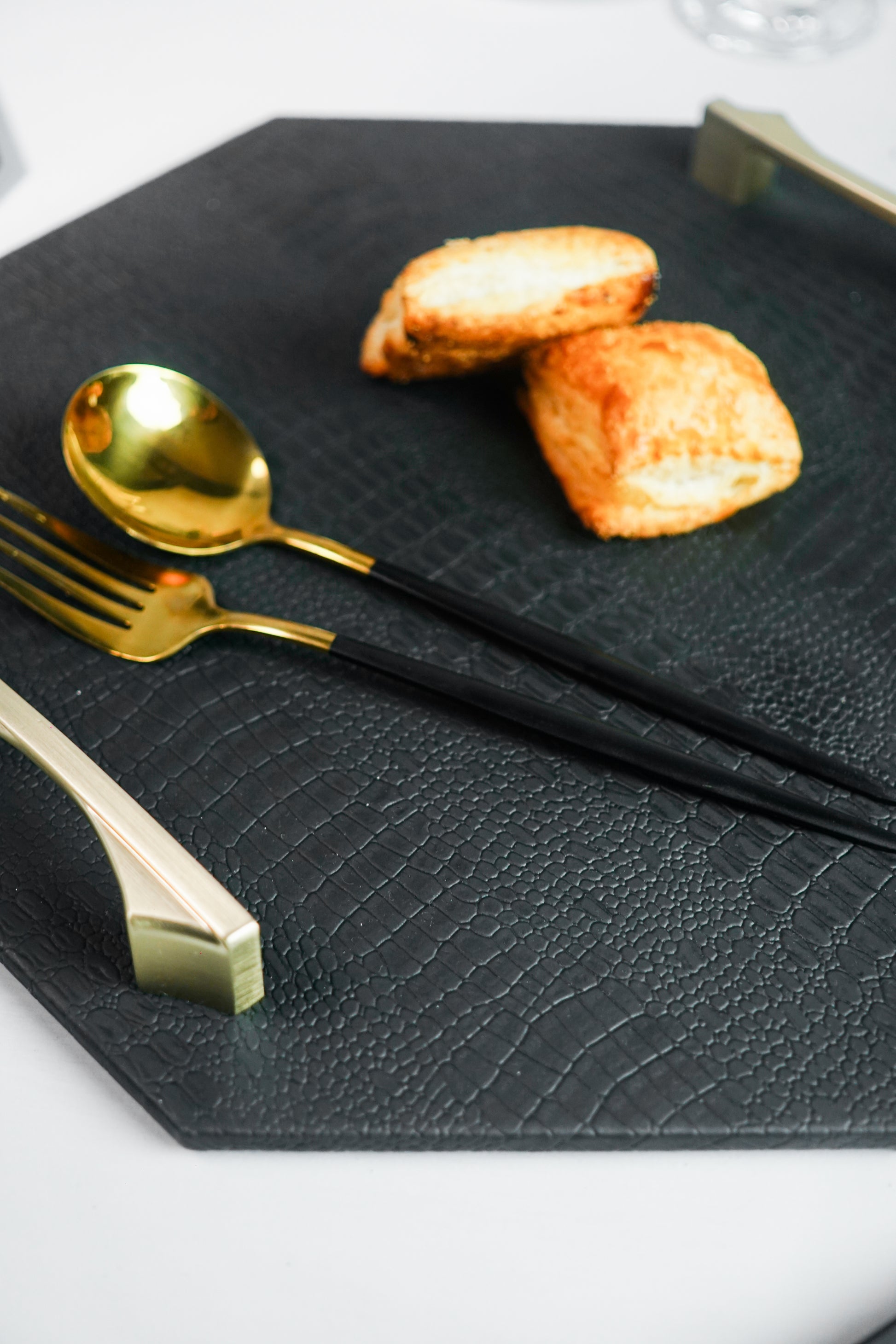 Close-up of a black octagon serving tray with a spoon and two biscuits visible. The background is blurred, focusing on the tray and its contents.